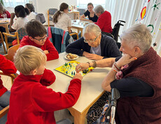 Jugendliche und Seniorinnen spielen ein Brettspiel und diskutieren über den nächsten Zug.