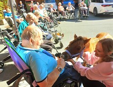 Ein Bewohner im Rollstuhl füttert Pony Maxi aus der Hand, während weitere Bewohnerinnen und Bewohner die Begegnung im sonnigen Innenhof des Pflegewohnhauses beobachten.