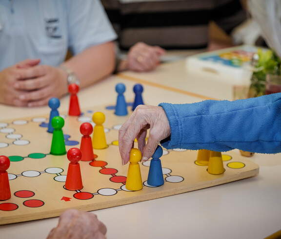 Bewohner*innen spielen gemeinsam mit einer Betreuerin "Mensch ärgere dich nicht".