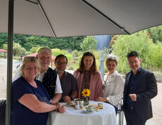 Sechs Erwachsene stehen lachend an einem Stehtisch im Gartenbereich des Hauses Suavitas.