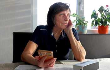 Frau sitzt am Tisch mit einem Handy in der Hand
