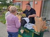 An einem Maronistand werden frisch gebratene Maroni in Papiertüten ausgegeben, während mehrere Personen im Freien auf der Terrasse zusammenkommen.