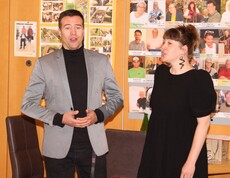Eine Dame und ein Herr aus dem Künstlerkollegium Manfred Grössler stehen nebeneinander und singen gemeinsam vor den Bewohnerinnen und Bewohnern des Caritas Pflegewohnhauses Graz-Straßgang. Beide wirken konzentriert und herzlich, während sie dem Publikum mit ihrer Darbietung eine Freude bereiten. Im Vordergrund sind einige Zuhörer*innen zu sehen, die aufmerksam lauschen.
