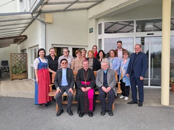 Gruppenfoto vor dem Eingang des Pflegewohnhauses mit Teilnehmenden eines Besuchs, die gemeinsam im Außenbereich versammelt sind.