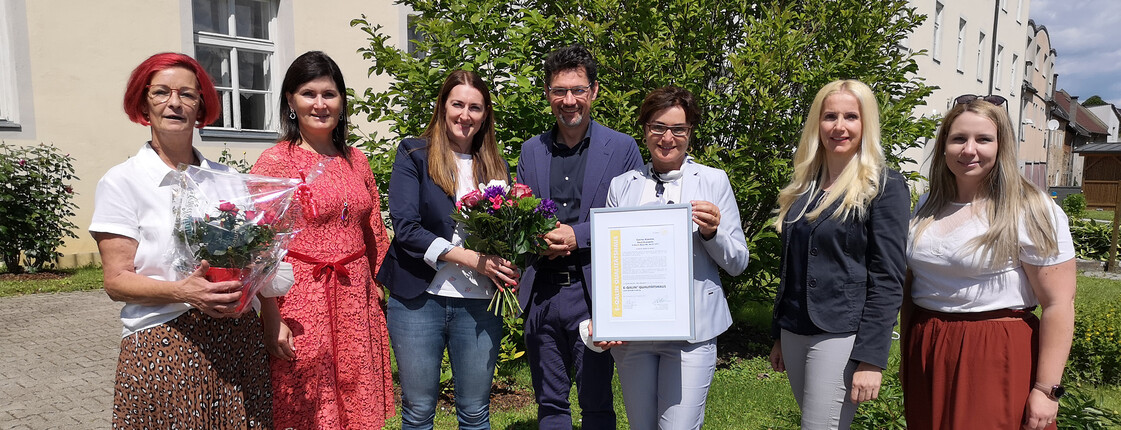 Mitarbeiter*innen des Pflegewohnhaus "Haus Elisabeth" präsentieren gemeinsam mit Beate Prettner, Caritasdirektor Ernst Sandriesser und Bereichsleiterin Donata Rössler-Merlin das Zertifikat E-Qalin.