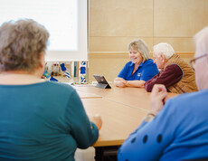 Senior*innenrunde mit Betreuungskraft vor Präsentation und Tablet