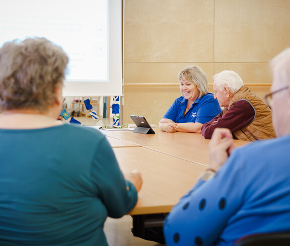 Senior*innenrunde mit Betreuungskraft vor Präsentation und Tablet