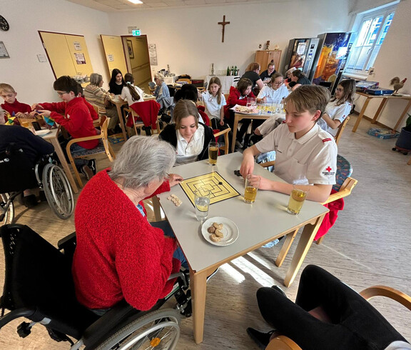 Jugendliche und Bewohner*innen spielen Mühle, während weitere Gruppen im Saal Brettspiele spielen.
