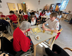 Jugendliche und Bewohner*innen spielen Mühle, während weitere Gruppen im Saal Brettspiele spielen.