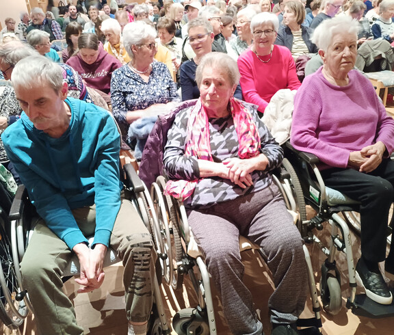 Mehrere Bewohner*innen des Haus Michael sitzen mit Rollstühlen im voll besetzten Saal.