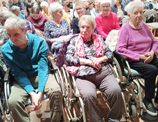 Mehrere Bewohner*innen des Haus Michael sitzen mit Rollstühlen im voll besetzten Saal.