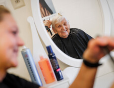 Im Spiegel sieht man eine glückliche Dame, der gerade die Haare geschnitten werden.