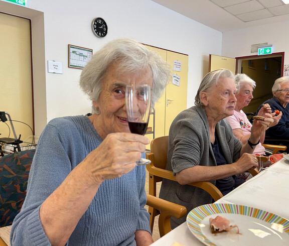 Bewohner*in hält ein Glas Rotwein während der Weinverkostung im Haus Franziskus.