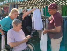 Seniorin im Rollstuhl zahlt an einem Kleidungsstand, begleitet von zwei Frauen
