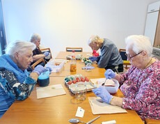 Bewohner*innen färben Ostereier in Schüsseln mit verschiedenen Farben an einem Tisch.