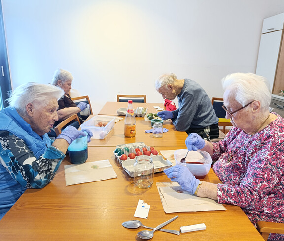 Bewohner*innen färben Ostereier in Schüsseln mit verschiedenen Farben an einem Tisch.