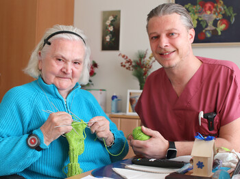 Ein Pfleger strickt mit einer Seniorin.