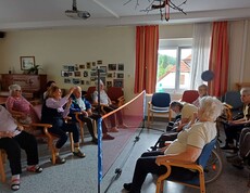 Bewohner*innen des Caritas Pflegewohnhauses Lannach sitzen auf Stühlen und in Rollstühlen. Sie werfen sich einen Softball über ein niedriges Netz zu – konzentriert, lachend und mit sichtbarer Freude an der Bewegung