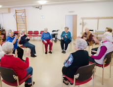 Senior*innen sitzen im Kreis und machen angeleitete Bewegungsübungen.