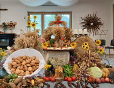Erntedank-Dekoration mit Brot, Obst, Gemüse, Getreide, Sonnenblumen und einem aus Ähren gestalteten Motiv.