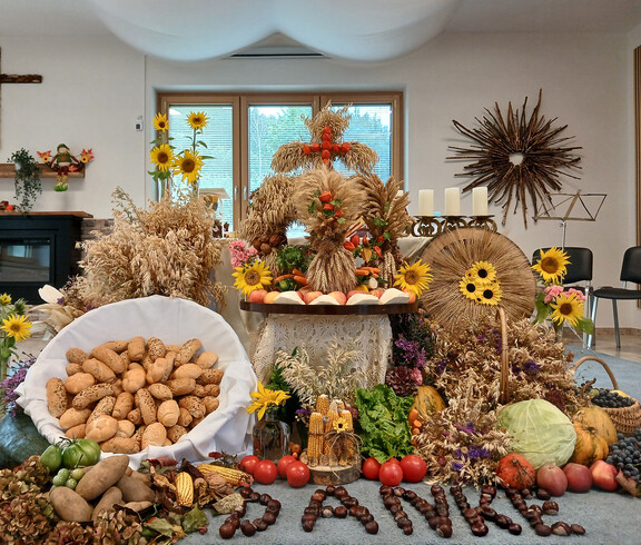 Erntedank-Dekoration mit Brot, Obst, Gemüse, Getreide, Sonnenblumen und einem aus Ähren gestalteten Motiv.