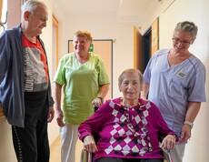 Zwei Bewohner*innen und zwei Pflegerinnen stehen am Gang.