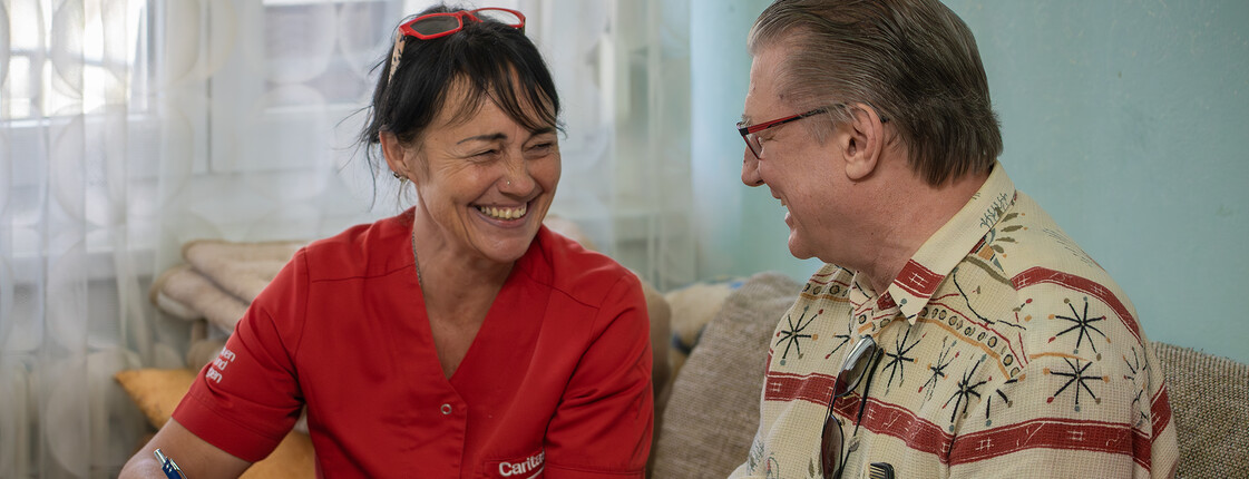 Eine Heimhelferin sitzt mit einem älteren Herrn am Esstisch und schreibt mit ihm die Einkaufsliste.