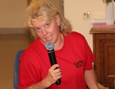 Eine blonde Frau trägt ein rotes „Caritas & Du“-Shirt und singt engagiert in ein Mikrofon.