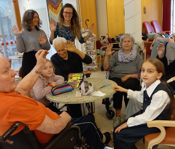 In einem Gemeinschaftsraum des Pflegewohnhauses sitzen Kinder und Bewohnende gemeinsam an einem Tisch beim kreativen Gestalten.