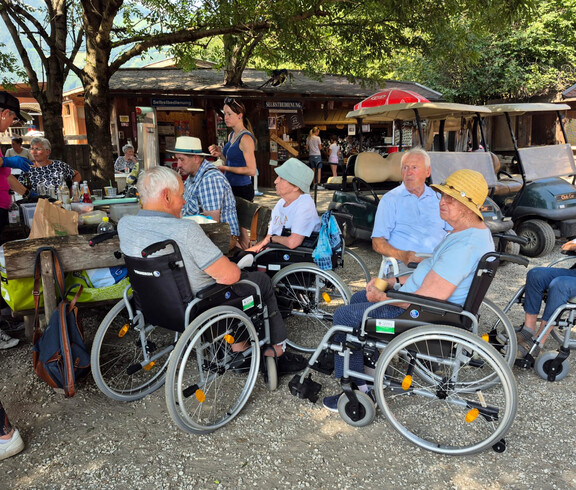 Senior*innen im Rollstuhl sitzen im Schatten bei einem Picknick im Eselpark.