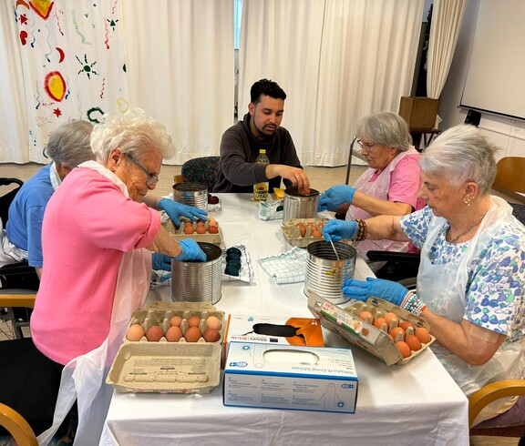 Bewohner*innen färben Ostereier mit Handschuhen und Töpfen an einem großen Tisch.