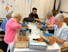 Bewohner*innen färben Ostereier mit Handschuhen und Töpfen an einem großen Tisch.