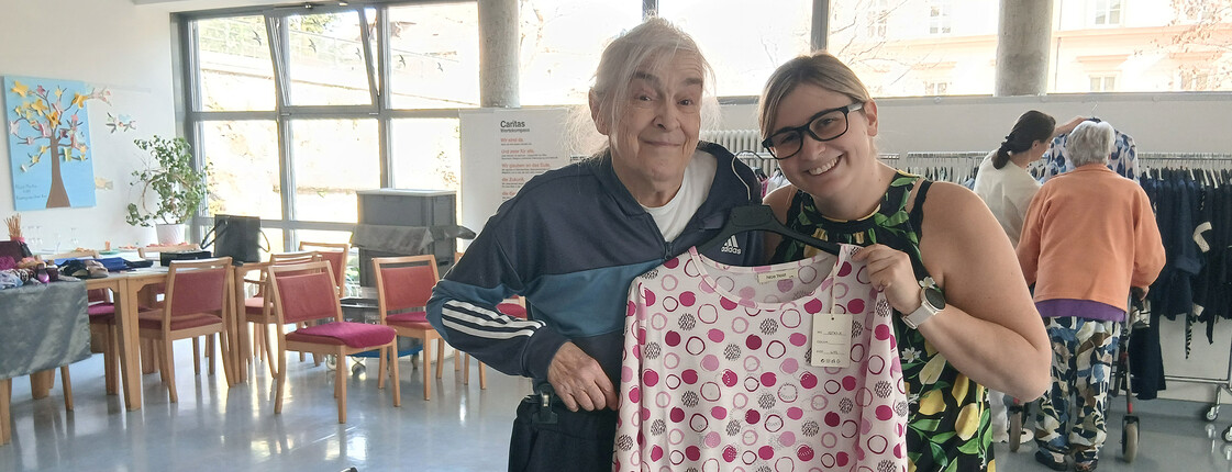 Bewohnerin und Mitarbeiterin halten ein pink gemustertes Oberteil in heller Umgebung