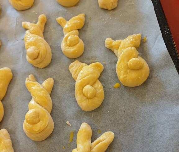 Frisch geformte Germteig‑Haserl liegen auf einem Backblech und sind bereits mit Ei bestrichen. Die verschiedenen Figuren warten darauf, im Pflegewohnhaus in den Ofen geschoben zu werden.