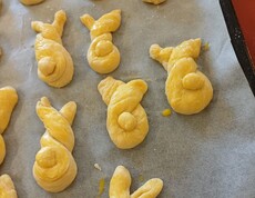 Frisch geformte Germteig‑Haserl liegen auf einem Backblech und sind bereits mit Ei bestrichen. Die verschiedenen Figuren warten darauf, im Pflegewohnhaus in den Ofen geschoben zu werden.