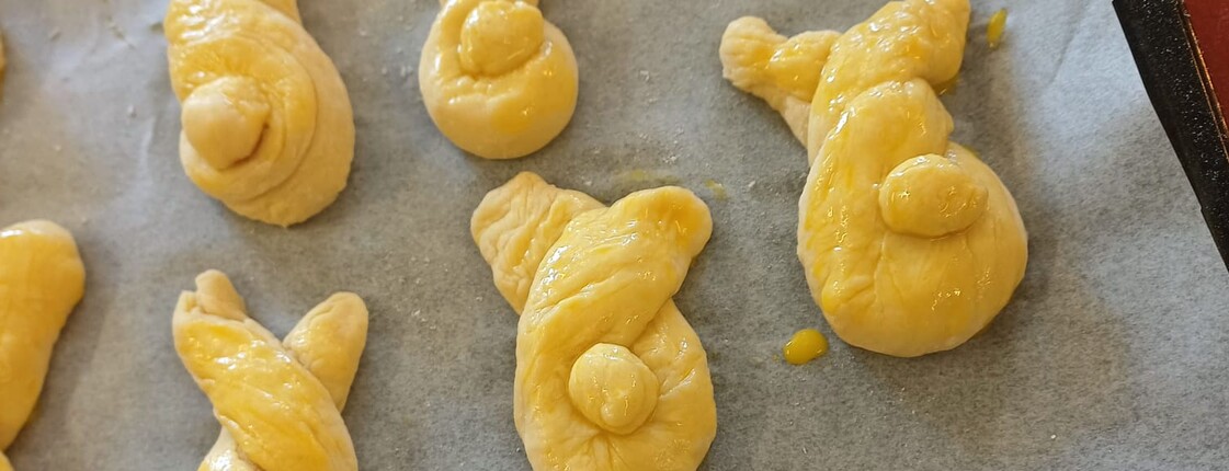 Frisch geformte Germteig‑Haserl liegen auf einem Backblech und sind bereits mit Ei bestrichen. Die verschiedenen Figuren warten darauf, im Pflegewohnhaus in den Ofen geschoben zu werden.