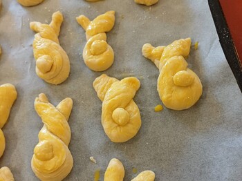 Frisch geformte Germteig‑Haserl liegen auf einem Backblech und sind bereits mit Ei bestrichen. Die verschiedenen Figuren warten darauf, im Pflegewohnhaus in den Ofen geschoben zu werden.