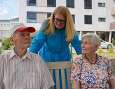 Zwei Bewohner*innen und die Pflegeleitung sitzen draußen auf einer Bank.