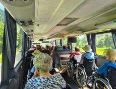 Senior*innen im Rollstuhl sitzen im Reisebus mit Blick auf die grüne Landschaft.
