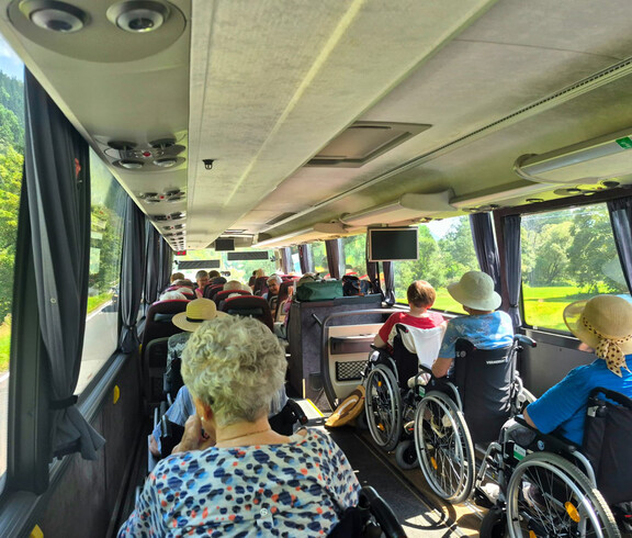 Senior*innen im Rollstuhl sitzen im Reisebus mit Blick auf die grüne Landschaft.