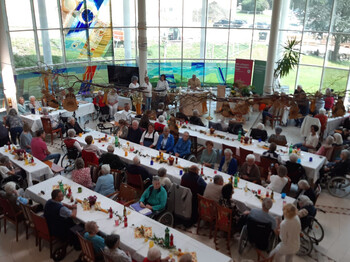 Festlich geschmückter Saal voller Bewohner*innen, Angehöriger und Gäste, die das Herbstfest gemeinsam genießen. Zahlreiche Senior*innen und Gäste sitzen an langen Tafeln beim Herbstfest im Haus Suavitas.