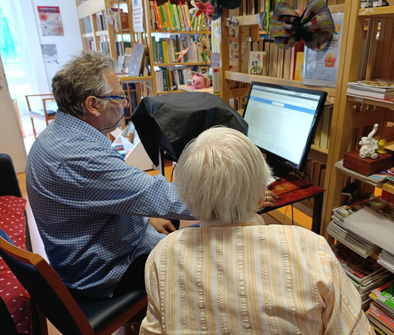 Zwei Personen sitzen vor einem Computerbildschirm in der Bücherei und lernen gemeinsam.
