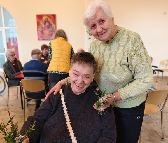 Bewohner*innen binden Palmbuschen aus Zweigen und Palmkätzchen an einem Arbeitstisch.