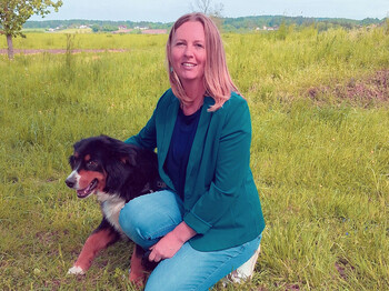 Eine Frau kniet mit einem Hund in einer Wiese.