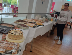 Frau präsentiert ein großes Kuchenbuffet mit Torten, Strudel und Mehlspeisen beim Herbstfest.