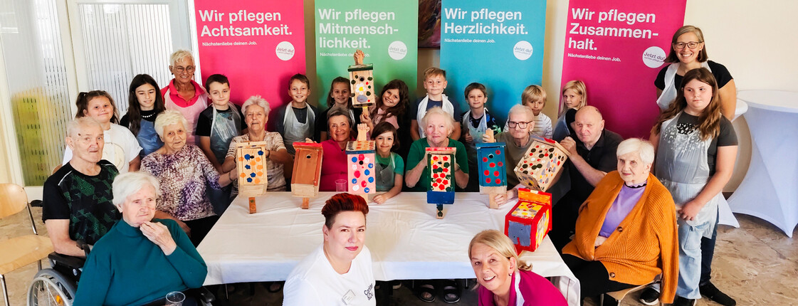 Senior*innen und Kinder posieren vor bunten Rollups mit selbstgebauten Vogelbrutkästen.