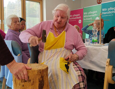 Bewohnerin mit Schürze schlägt konzentriert mit Hammer beim Nagelspiel auf Holzblock.