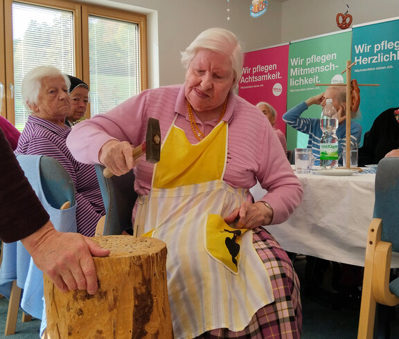 Bewohnerin mit Schürze schlägt konzentriert mit Hammer beim Nagelspiel auf Holzblock.