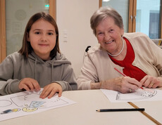 Kind und Senior*in sitzen am Tisch und malen Weihnachtsmotive aus