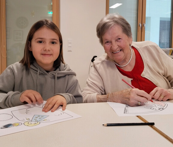 Kind und Senior*in sitzen am Tisch und malen Weihnachtsmotive aus